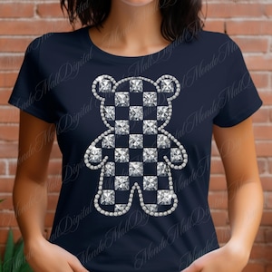 May include: Navy blue t-shirt featuring a sparkling, checkered teddy bear design. The bear is outlined with shimmering accents, creating a dazzling effect. This tee is a stylish addition to any wardrobe.