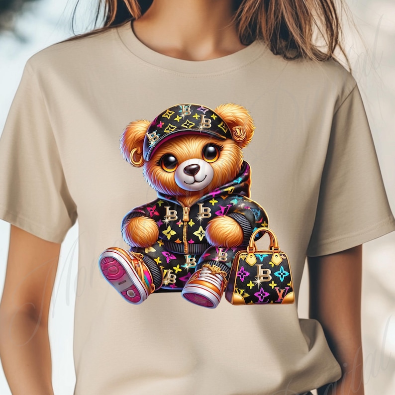 May include: A beige t-shirt with a cartoon illustration of a teddy bear wearing a black and white patterned jacket, a black and white patterned hat, and holding a black and white patterned handbag. The bear is wearing colorful sneakers.