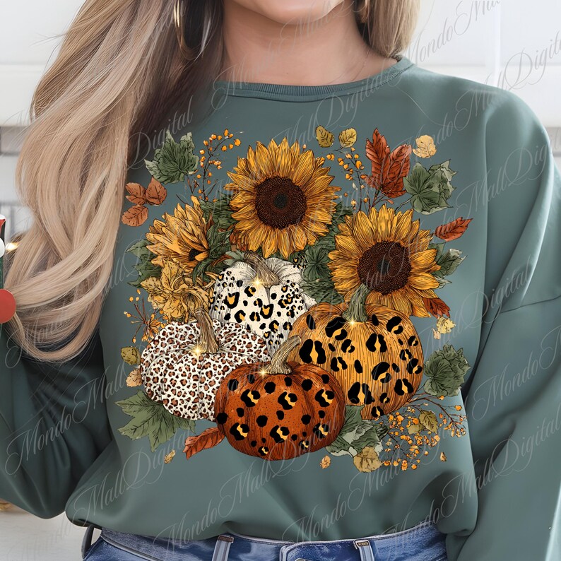 May include: A teal green sweatshirt featuring a fall-themed design. The design includes sunflowers, pumpkins with leopard print patterns, and autumn leaves. The pumpkins are orange, white, and brown. The sunflowers are yellow and brown.