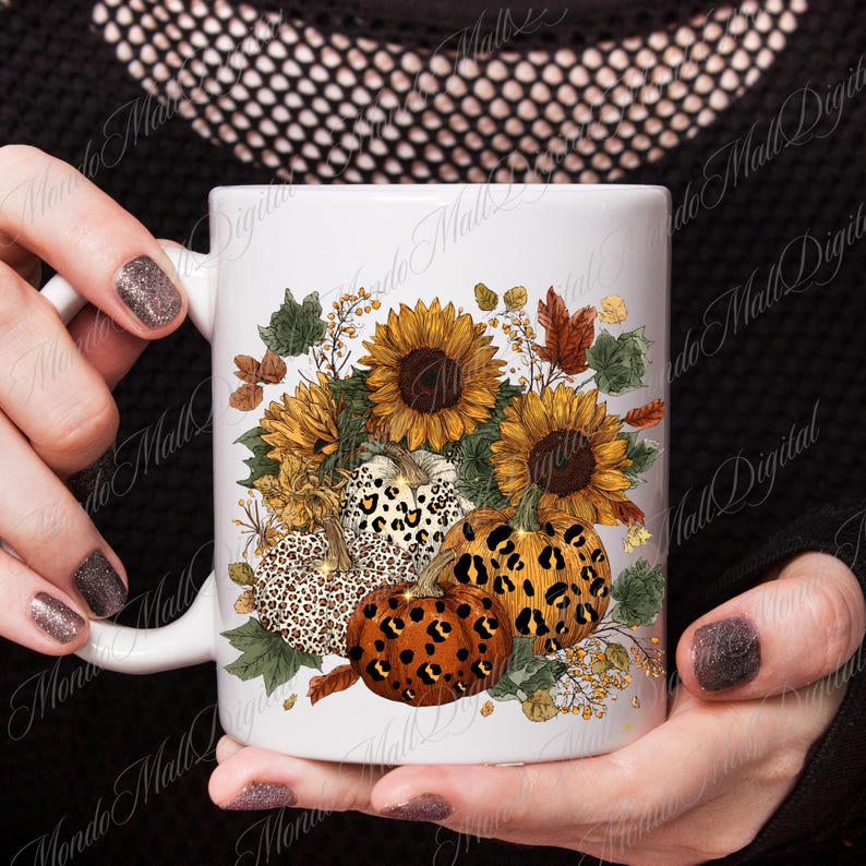 May include: White ceramic mug featuring a fall-themed design. The design includes sunflowers, pumpkins with leopard print patterns, and autumn leaves in shades of orange, brown, and yellow. The mug is held by a person.