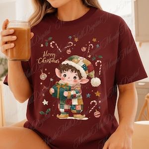 Op de afbeelding: Bordeauxrode crewneck t-shirt met een kerstelf-afbeelding die een cadeau vasthoudt. De elf draagt een patchwork outfit en hoed, omringd door zuurstokken, sterren en ornamenten. De tekst "Merry Christmas" is ook afgebeeld.