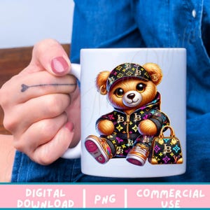 May include: A white ceramic mug with a colorful cartoon illustration of a teddy bear wearing a black and gold jacket and a hat with the letter "B" on it. The teddy bear is holding a black and gold handbag with the letter "B" on it. The mug is on a blue denim background.