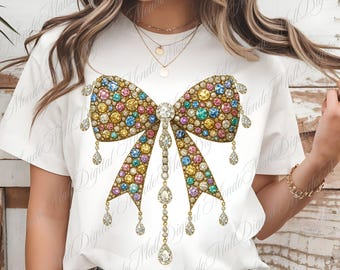 May include: White t-shirt featuring a large, ornate bow design. The bow is embellished with a multitude of colorful gemstones and dangling crystal accents. The design is centered on the shirt, creating a striking visual.