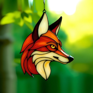 May include: A stained glass fox head ornament with a red, orange, and yellow color scheme. The fox's eyes are yellow and the background is green.