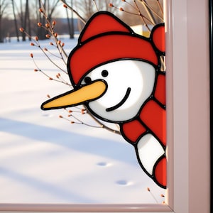 May include: A stained glass snowman peeks from behind a window frame. The snowman has a red hat and scarf, a white face, a yellow carrot nose, and a smiling black mouth. The background shows a snowy landscape with bare branches.