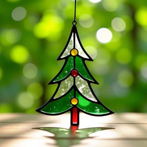 Könnte beinhalten: Ein Weihnachtsbaumschmuck aus Glasmalerei. Der Baum ist grün mit gelben und roten Akzenten und einer schwarzen Umrandung. Der Schmuck hängt vor einem verschwommenen grünen Hintergrund.