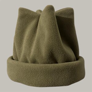 May include: Olive green fleece beanie hat with a folded brim and a unique, pointed crown design. The hat is made of a soft, textured material, perfect for cold weather. A stylish and warm winter accessory.
