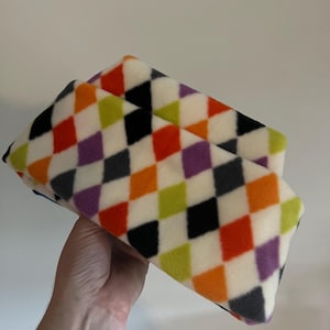 Peut inclure: Un tissu en polaire blanc avec un motif en losanges noir, orange, violet, vert et gris.