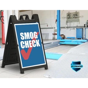 May include: A black A-frame sign with a blue and white sign that says "SMOG CHECK" in white letters with a red checkmark. The sign is UV printed and is in front of a garage.