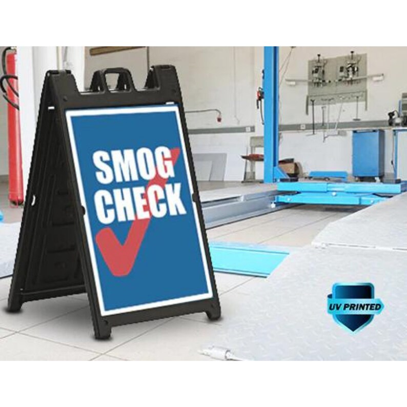 May include: A black A-frame sign with a blue and white sign that says "SMOG CHECK" in white letters with a red checkmark. The sign is UV printed and is in front of a garage.