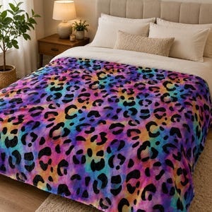 May include: A colorful leopard print blanket in shades of purple, blue, orange, and pink. The blanket features a repeating pattern of black leopard spots. The blanket is draped over a bed with white bedding.