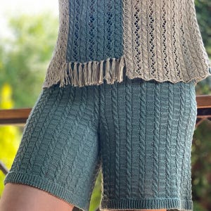 May include: A two-piece knitted outfit in shades of teal and beige. The top features a fringed hem and openwork design, while the shorts have a cable knit pattern. The outfit is made of a soft, breathable material.