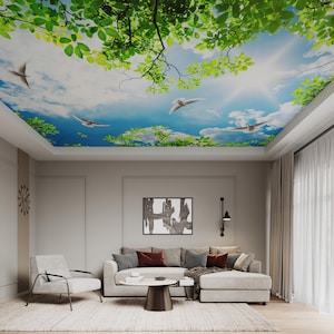 May include: A living room with a ceiling mural depicting a bright blue sky, white clouds, green leaves, and flying birds. The room features a light gray sofa, a white armchair, and a dark brown coffee table. The walls are a neutral beige color.