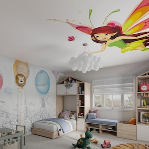 May include: A child's bedroom with a white ceiling featuring a colorful fairy decal. The room has a white bed with blue bedding, a wooden bookshelf, and a window with a white blind. The wall has a mural of hot air balloons and a lion.