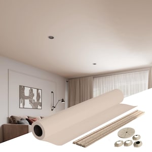 Puede incluir: Un panel de techo beige enrollado con un borde blanco, rieles metálicos y soportes de montaje de plástico blanco. El panel se muestra en una habitación con un sofá y una imagen en la pared.