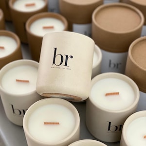 May include: A collection of cream-colored candles with wooden wicks. The candles are in cylindrical containers, some with lids. The text "br" is printed on the front of the candle, with "MINT / EUCALYPTUS / ROSE" below it.