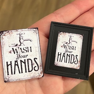 May include: Two miniature signs with the text "WASH Your HANDS". One sign is unframed, the other is in a black frame. Both signs feature a vintage-style faucet illustration and a distressed, aged appearance.