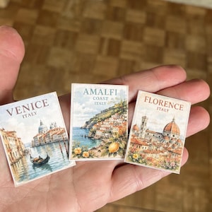 May include: Three small rectangular cards featuring watercolour-style illustrations of Italian cities. The left card shows Venice with a gondola, the centre card depicts the Amalfi Coast with lemons, and the right card displays the Florence skyline.