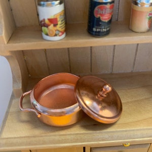 May include: A copper pot with a lid, the lid is off and the pot is sitting on a wooden surface.