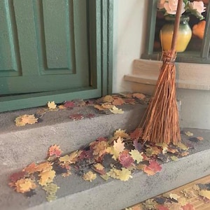 May include: A brown broom with a wooden handle sits on a set of concrete steps. The steps are covered in a scattering of colourful autumn leaves.