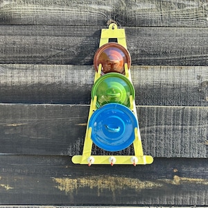 May include: A yellow metal rack with three round pot lids. The lids are brown, green, and blue.