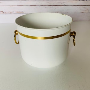 Könnte beinhalten: Weißer Metalltopf mit goldener Verzierung und zwei Messinggriffen.