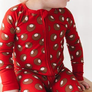 May include: A long-sleeved, full-length one-piece sleeper with a zipper closure down the front. The garment is bright red and features a repeating pattern of brown circles, each containing a smaller, off-white circular accent in the center.