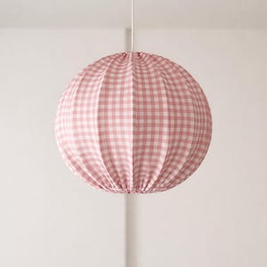 Könnte beinhalten: Ein runder Lampenschirm mit rosa-weißem Vichy-Muster hängt an einem weißen Kabel. Der Stoffschirm hat ein gerafftes Design und hängt vor einem weißen Hintergrund. Die Leuchte ist ein dekoratives Element für die Inneneinrichtung.