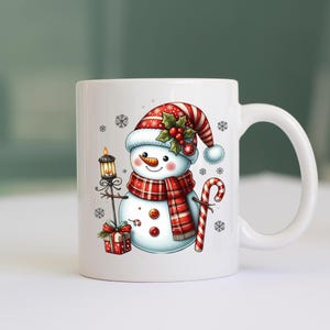 May include: White ceramic mug with a snowman design. The snowman is wearing a red and white hat with holly and berries, a red and black plaid scarf, and holding a candy cane. The snowman is also holding a lantern with a lit candle.