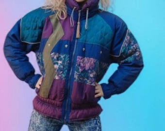 May include: A vintage-style quilted jacket in shades of blue, purple, and floral patterns. The jacket has a high collar and a zipper closure. The model is wearing acid wash jeans. The background is a gradient of pink and blue.