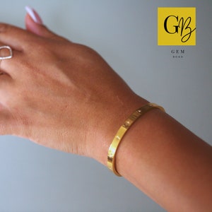 May include: Gold bangle bracelet with small round accents. The bracelet is on a person's wrist.