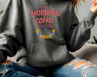 May include: A gray hoodie with a pink and white graphic that says "my daily morning coffee routine". Two cartoon coffee cups are walking across a crosswalk.