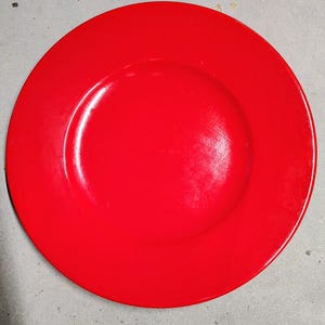 Puede incluir: Un plato de cena rojo liso con un acabado brillante. El plato tiene un borde ancho y un centro ligeramente hundido. Esta vajilla es adecuada para el uso diario o para ocasiones especiales.