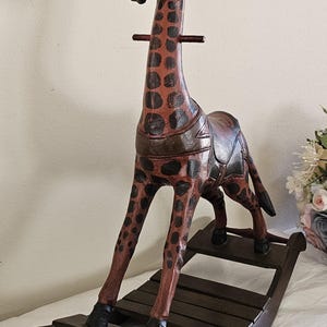 May include: A wooden rocking giraffe toy with a brown and black spotted pattern. The giraffe has a long neck, a saddle, and is mounted on a wooden rocker base. The toy is designed for children.
