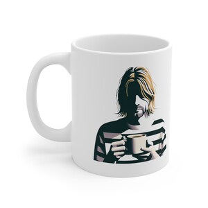 May include: White ceramic mug with a graphic of a person with long blonde hair wearing a striped shirt and holding a coffee mug. The person's face is obscured by shadows.