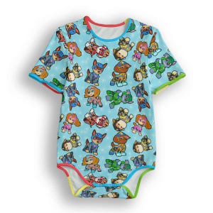 Pode incluir: Um body de bebê azul claro com um padrão colorido de cães de desenho animado em várias poses. O body tem mangas curtas e acabamentos em vermelho, azul, verde e amarelo. O fundo tem pequenas estrelas brancas.