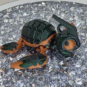 May include: A 3D printed toy turtle with a green and orange shell. The turtle has a detailed design and is sitting on a bed of clear crystals.