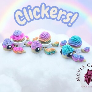 May include: A collection of colorful, whimsical Clickers! figurines. Each figurine features a cupcake-like design with rainbow-colored frosting and a snail-like body. The text "Clickers!" is displayed above the figurines, with a rainbow in the background.