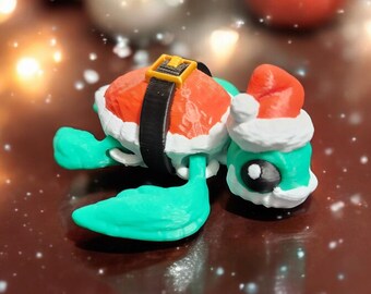 May include: A teal green turtle wearing a red and white Santa hat and a black belt with a gold buckle. The turtle is lying on its back on a brown surface.