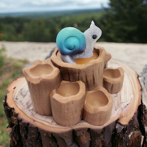 May include: A wooden tree stump with a snail figurine on top. The snail is blue and green with a silver shell. The stump has five small holes around the base.