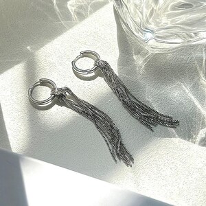 以下が含まれることがあります： 長いチェーンがぶら下がった、銀色のフープイヤリングのペア。チェーンは、小さな金属製のリンクの複数のストランドでできています。