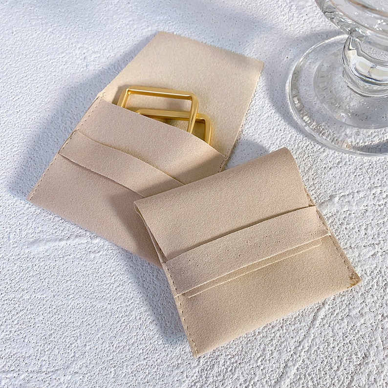 Pode incluir: Duas bolsas de feltro bege, uma com uma fivela de metal dourado no interior e a outra vazia.