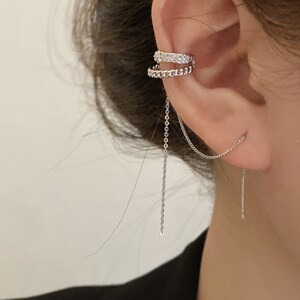 Pode incluir: Um brinco de argola prateado com uma corrente pendurada. A argola &eacute; decorada com pequenos strass transparentes. A corrente est&aacute; presa a um pequeno brinco de press&atilde;o prateado.