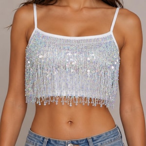 May include: White crop top with thin straps and a beaded fringe. The fringe is made of iridescent beads and sequins, creating a shimmering effect. The top is a stylish piece of clothing.