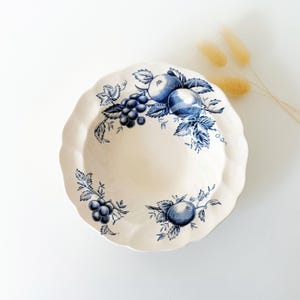 Pode incluir: Prato de cerâmica creme com borda ondulada, adornado com um design de frutas e folhas azuis. O prato apresenta ilustrações de maçãs e uvas, criando uma estética clássica e vintage. Uma peça decorativa para servir ou expor.