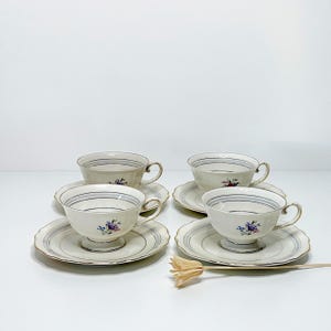 Peut inclure: Quatre tasses et soucoupes à thé vintage. Les tasses et les soucoupes sont de couleur crème avec un motif rayé bleu et gris et une bordure dorée. Chaque tasse présente un petit bouquet floral. Un service à thé classique.