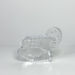 Peut inclure: Une figurine d'éléphant en verre transparent avec une surface texturée. L'éléphant est en position assise, sa trompe recourbée vers le haut. La figurine présente un design détaillé, avec les oreilles, les yeux et un motif en forme de selle sur le dos.