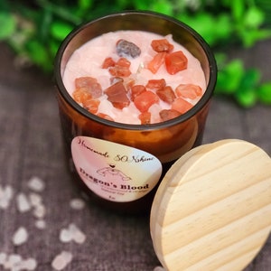 May include: A brown glass candle jar with a pink wax candle and red crystals inside. The jar has a wooden lid and a label that says "Homemade So Shine Dragon's Blood".