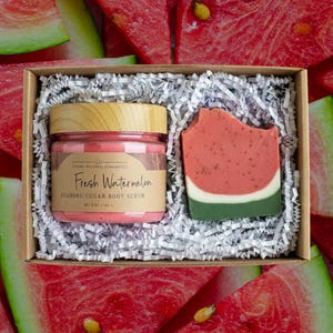 May include: A gift set containing a jar of pink foaming sugar body scrub and a watermelon-themed soap bar. The jar has a wooden lid and a label that reads "Fresh Watermelon". The soap is red, white, and green, resembling a watermelon slice.