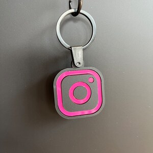 May include: A black and pink Instagram logo keychain with a silver metal ring.